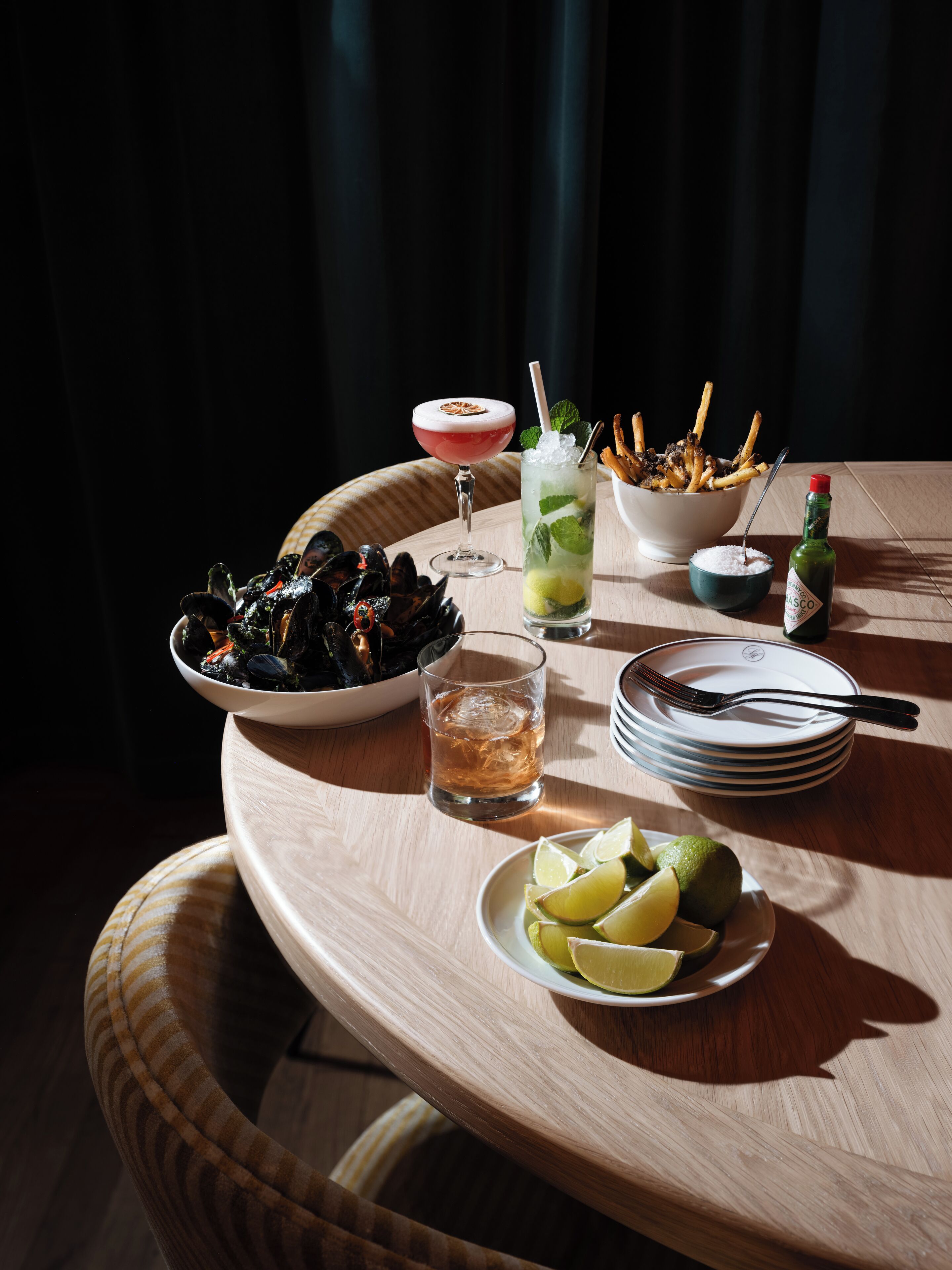 Una mesa de comedor con diversos platos, incluyendo mariscos, un cóctel y una botella de vino.