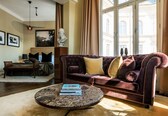 A living room with a dark purple sofa, a round coffee table with books, a wooden bench, and a bust sculpture.