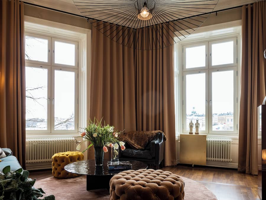 Un soggiorno accogliente con una grande finestra, un divano nero, un tavolino rotondo e una lampada decorativa.