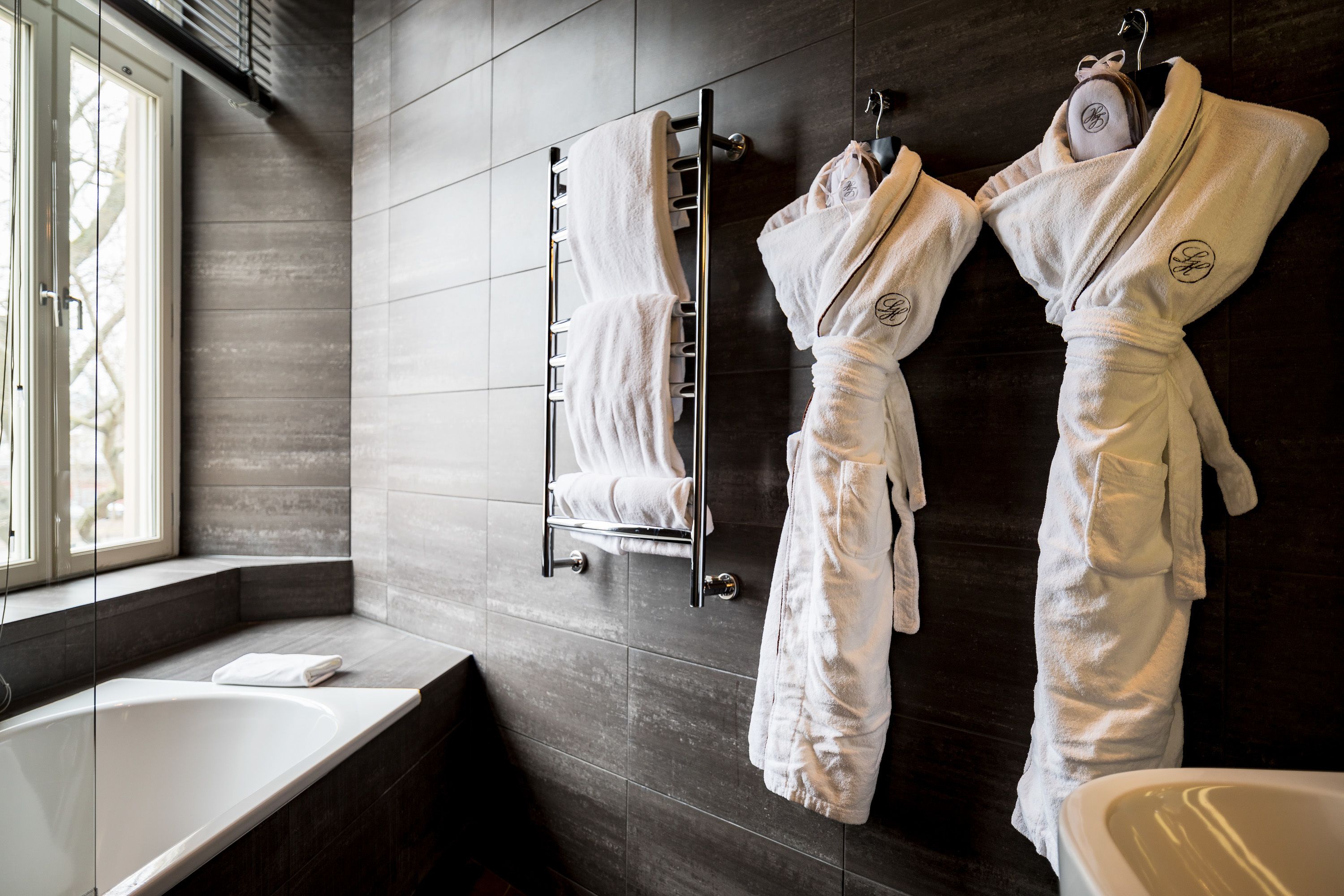 Un baño moderno con una bañera, un perchero con dos albornoces blancos y un espejo.