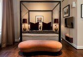 A bedroom with a four-poster bed, two bedside lamps, a television, and a framed picture on the wall.