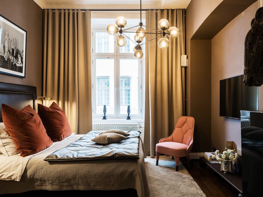 Ein Schlafzimmer mit einem Bett, einem Sessel, einem Fernseher und einem Fenster mit Vorhängen.