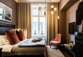 A bedroom with a bed, a chair, a TV, and a window with curtains.