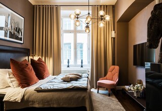 A bedroom with a bed, a chair, a TV, and a window with curtains.