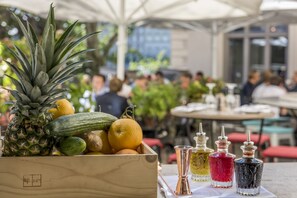 A wooden crate filled with fruits and vegetables, a table with cocktail glasses, and a blurred background of people dining.