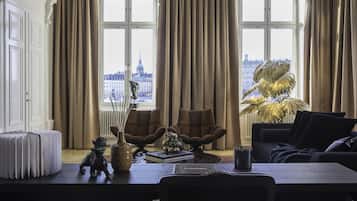 A room with a view of a cityscape, featuring a large window, a sofa, a table with a vase and a book, and a radiator.