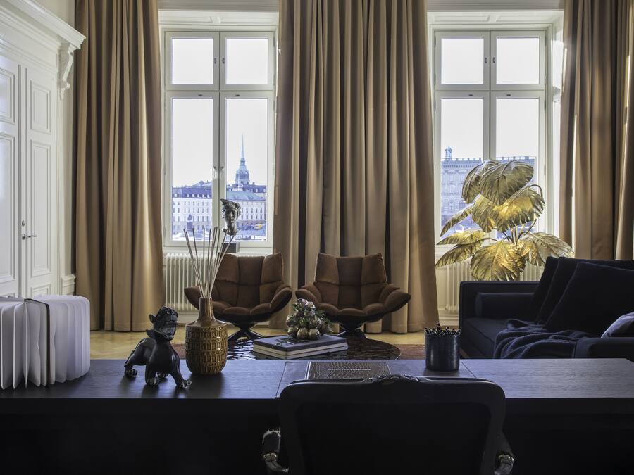 Une pièce avec vue sur la ville, comprenant une grande fenêtre, un canapé, une table avec un vase et un livre, ainsi qu’un radiateur.