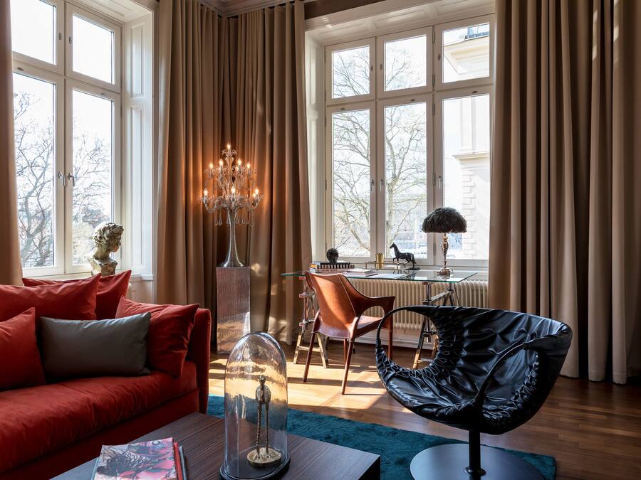A modern living room with a red sofa, a glass coffee table, a black leather chair, and a dining area with a table and chairs.