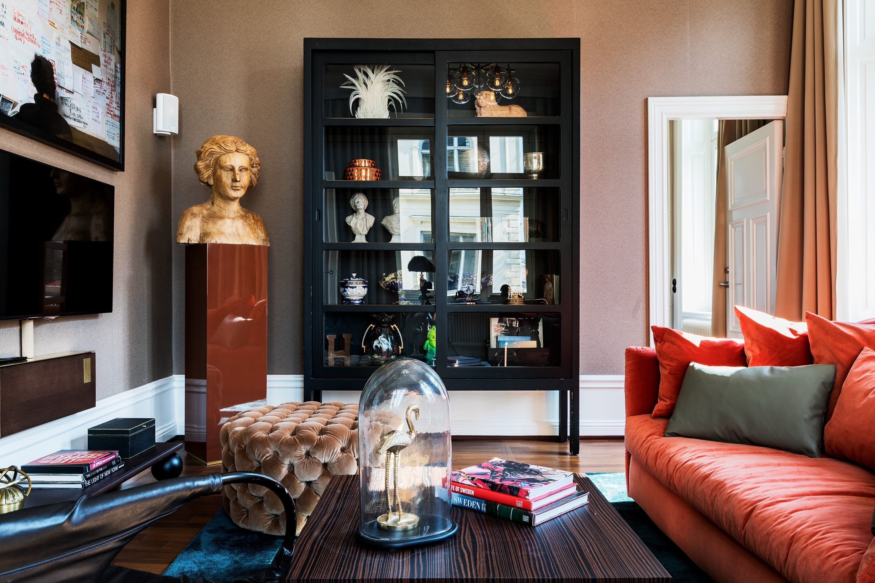 A living room with a red sofa, a glass dome with an object inside, a black bookshelf, and a bust on a pedestal.