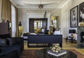 A modern living room with a dark sofa, a black coffee table, and a large black rug. There is a fireplace with a mantel and a mirror above it.