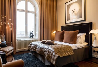 A bedroom with a large bed, a nightstand, a chair, and a window with curtains.