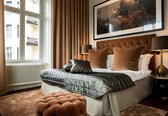A bedroom with a large bed, a tufted headboard, two bedside lamps, a window with curtains, and a framed picture on the wall.
