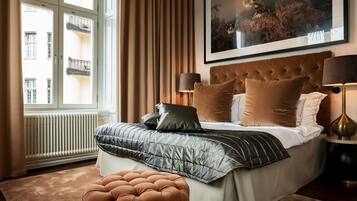 A bedroom with a large bed, a tufted headboard, two bedside lamps, a window with curtains, and a framed picture on the wall.