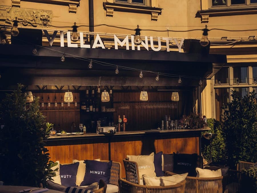 A bar area with a sign reading 'VILLA MINUTY,' wicker furniture, and a wooden bar counter.