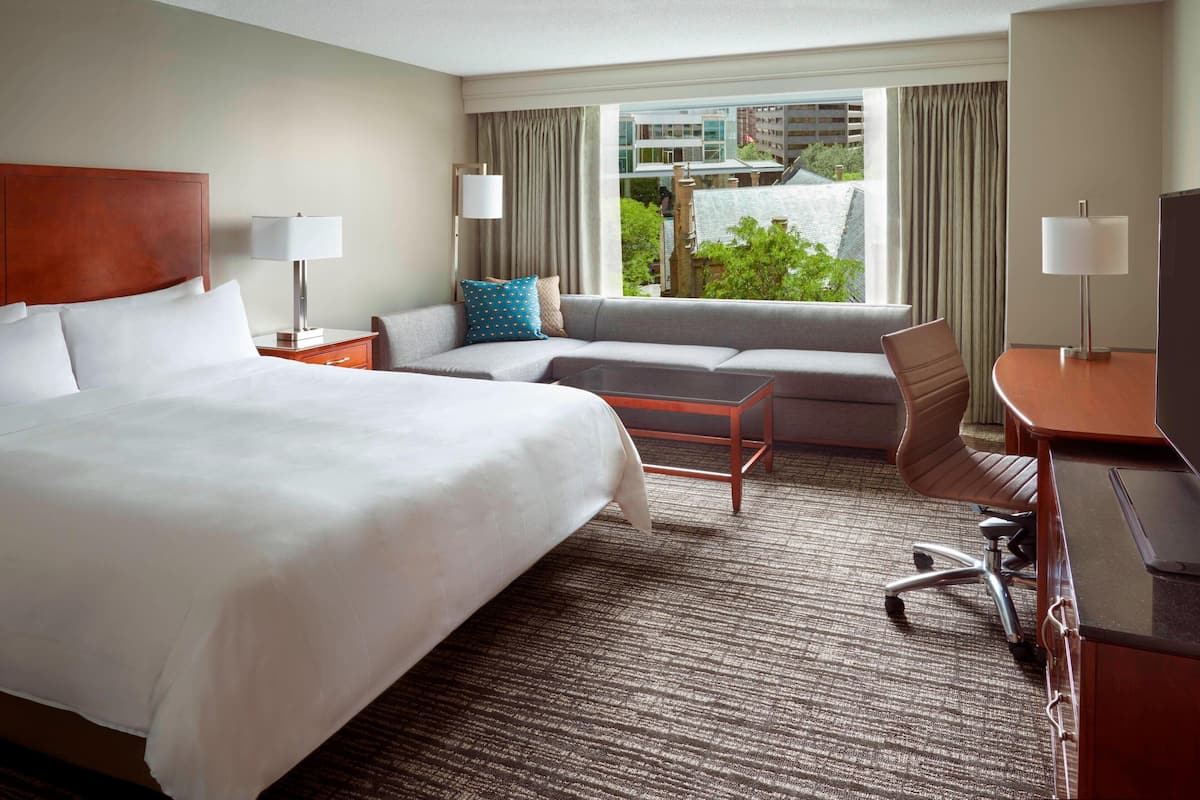 A hotel room with a large bed, a sofa, a desk, and a view of the outdoors.