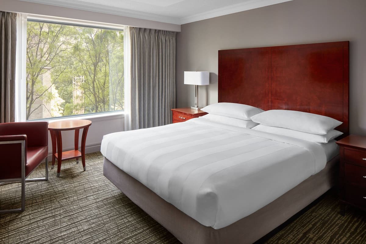 A hotel room with a large bed, a desk, a chair, and a window with curtains.