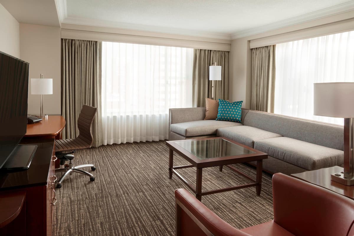 A hotel room with a sofa, armchair, and a glass coffee table.
