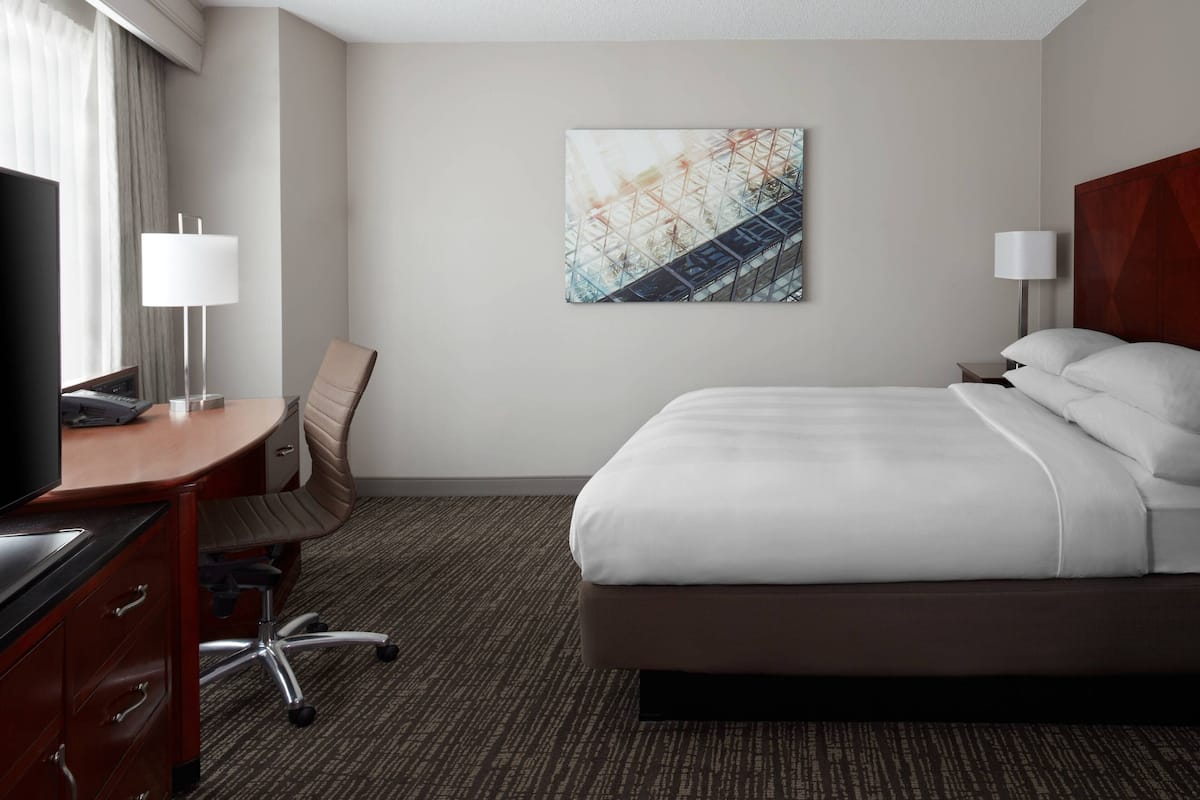 A hotel room with a bed, desk, chair, and artwork on the wall.