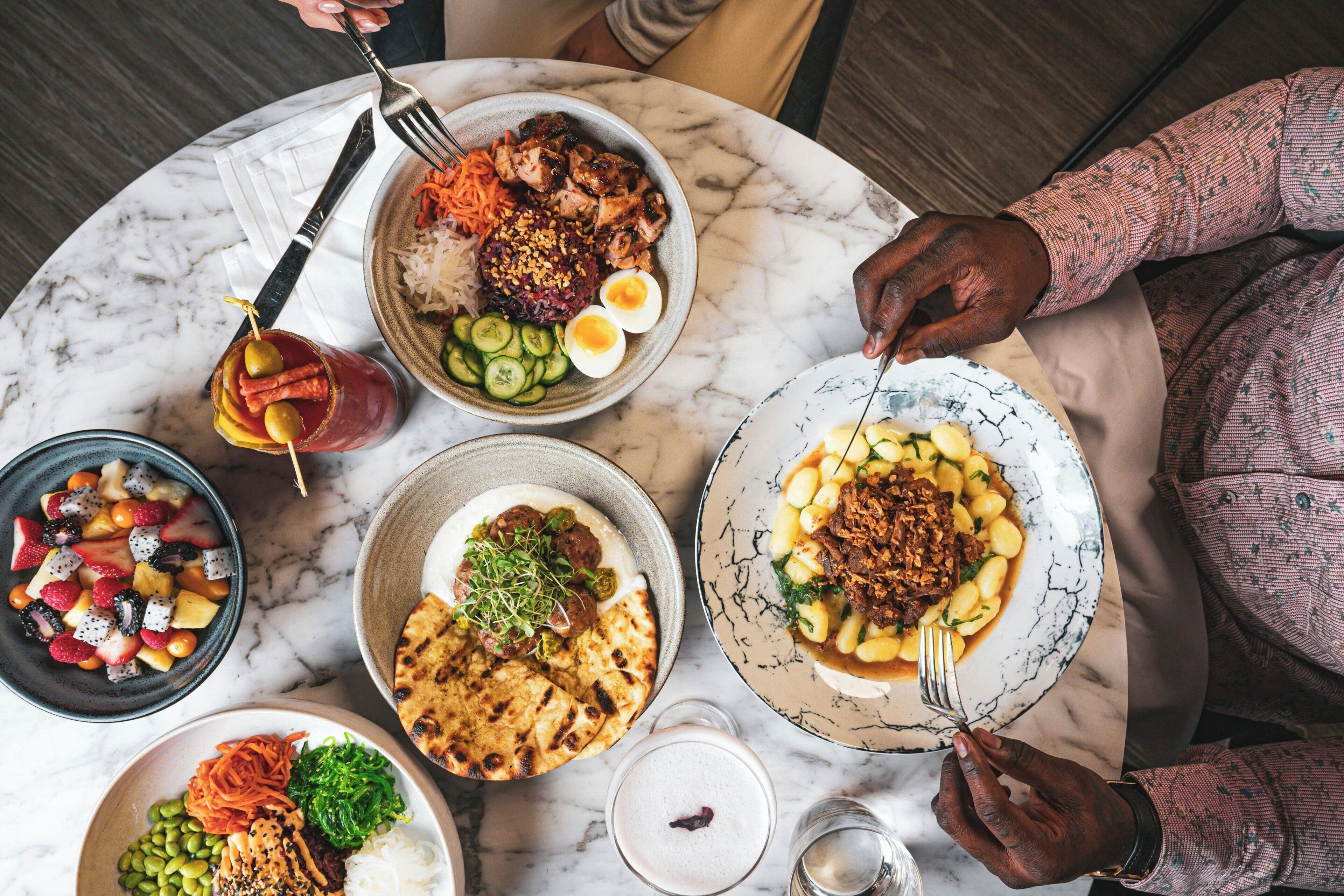 A table with various dishes including rice, vegetables, and meat, and a person is eating.