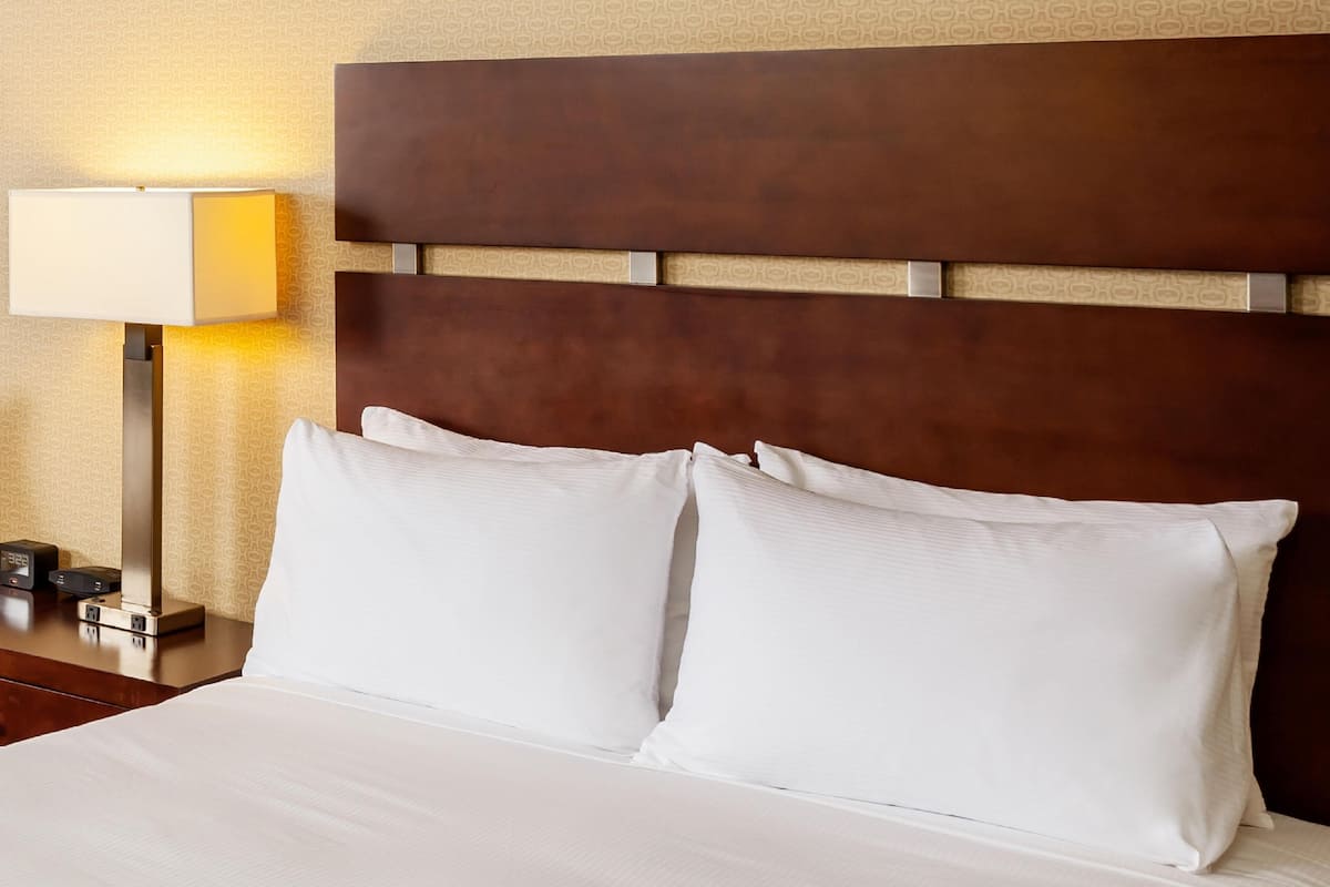 A neatly made bed with white linens, a wooden headboard, and a bedside lamp.