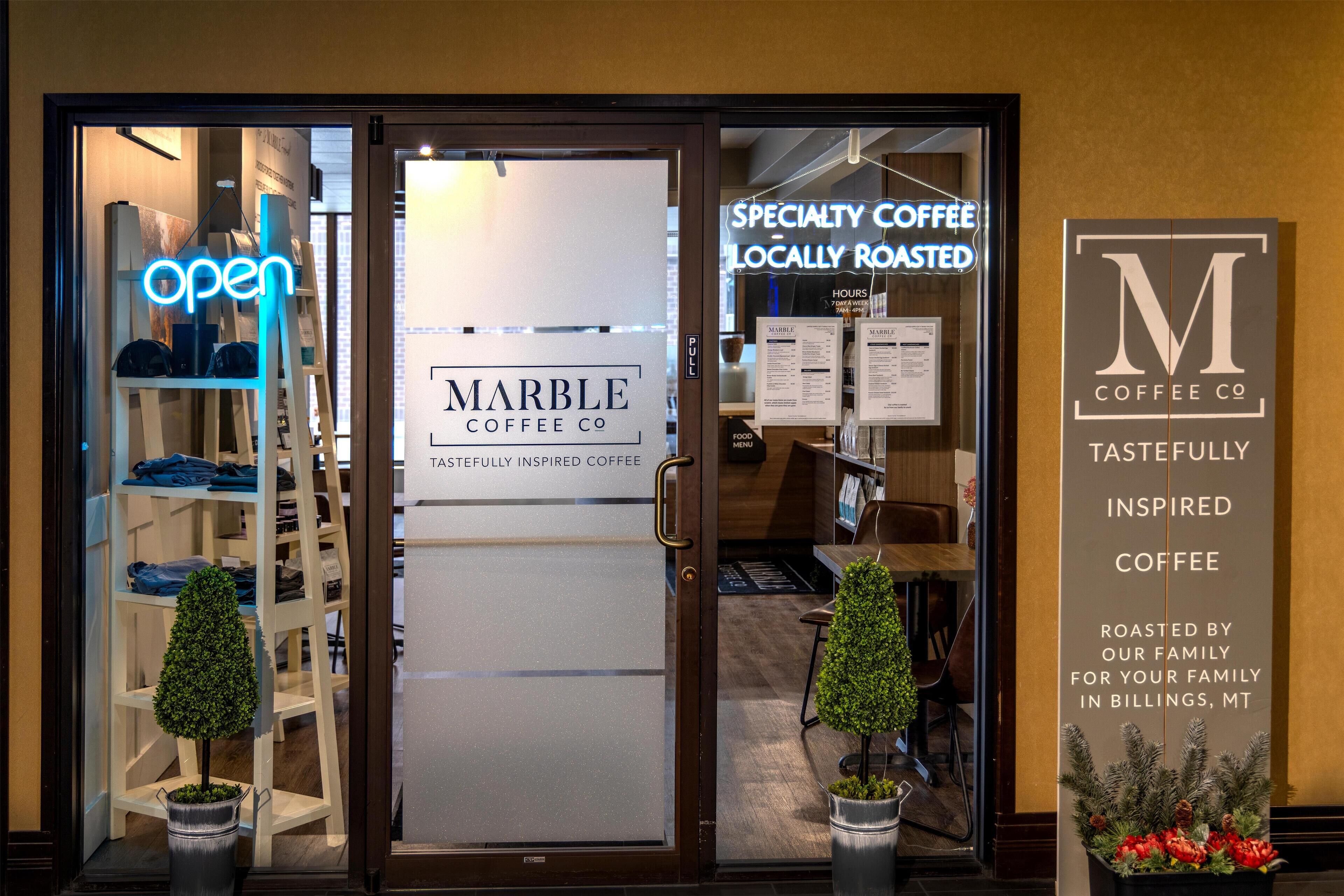 The entrance of Marble Coffee Co. with a neon 'OPEN' sign, a glass door, and a signboard stating 'Specialty Coffee Locally Roasted'.