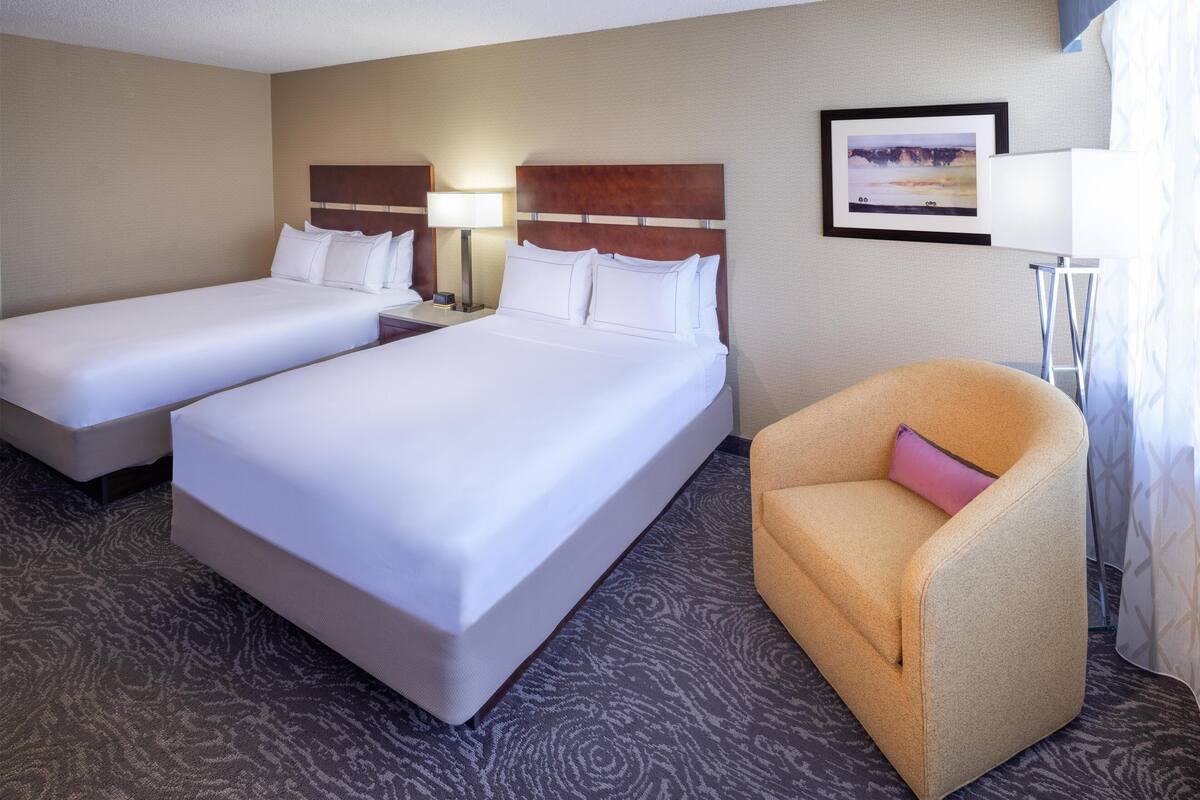 A hotel room with two single beds, a sofa, a nightstand with a lamp, and a framed picture on the wall.
