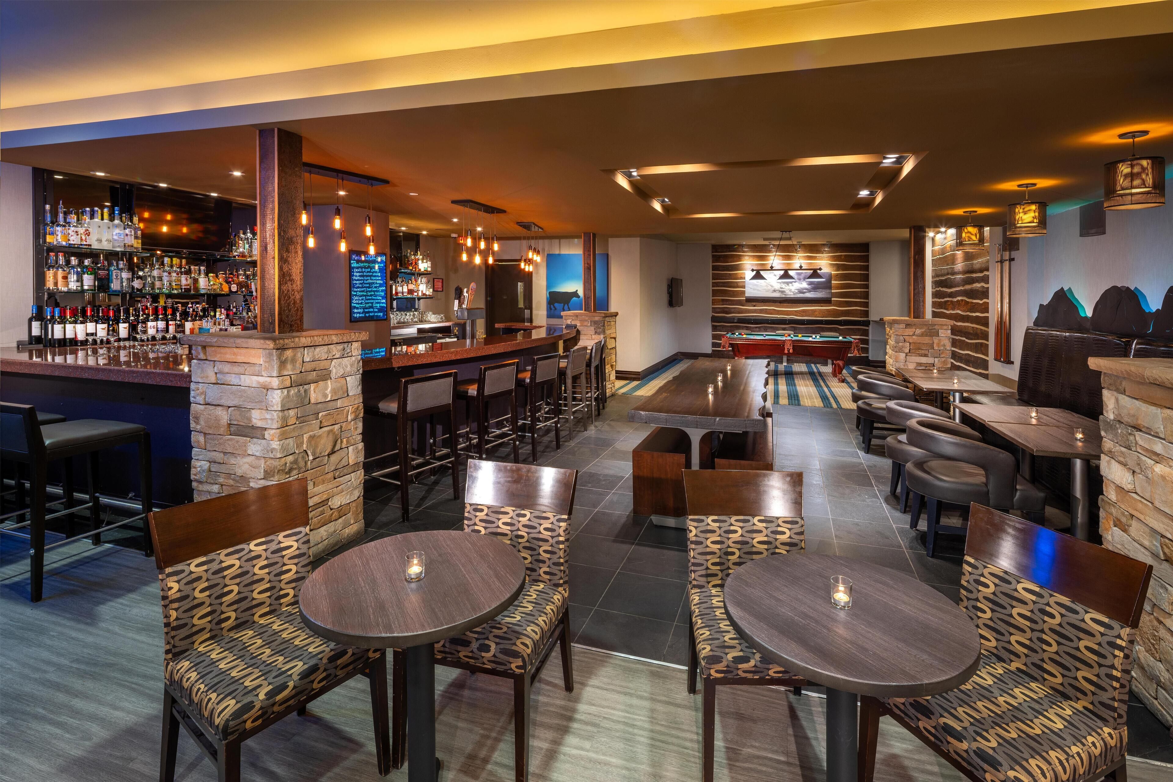 A bar area with a pool table, seating, and a bar stocked with bottles.