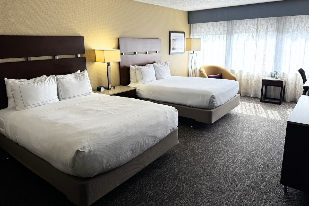 A hotel room with two beds, a desk, a chair, and a window with curtains.