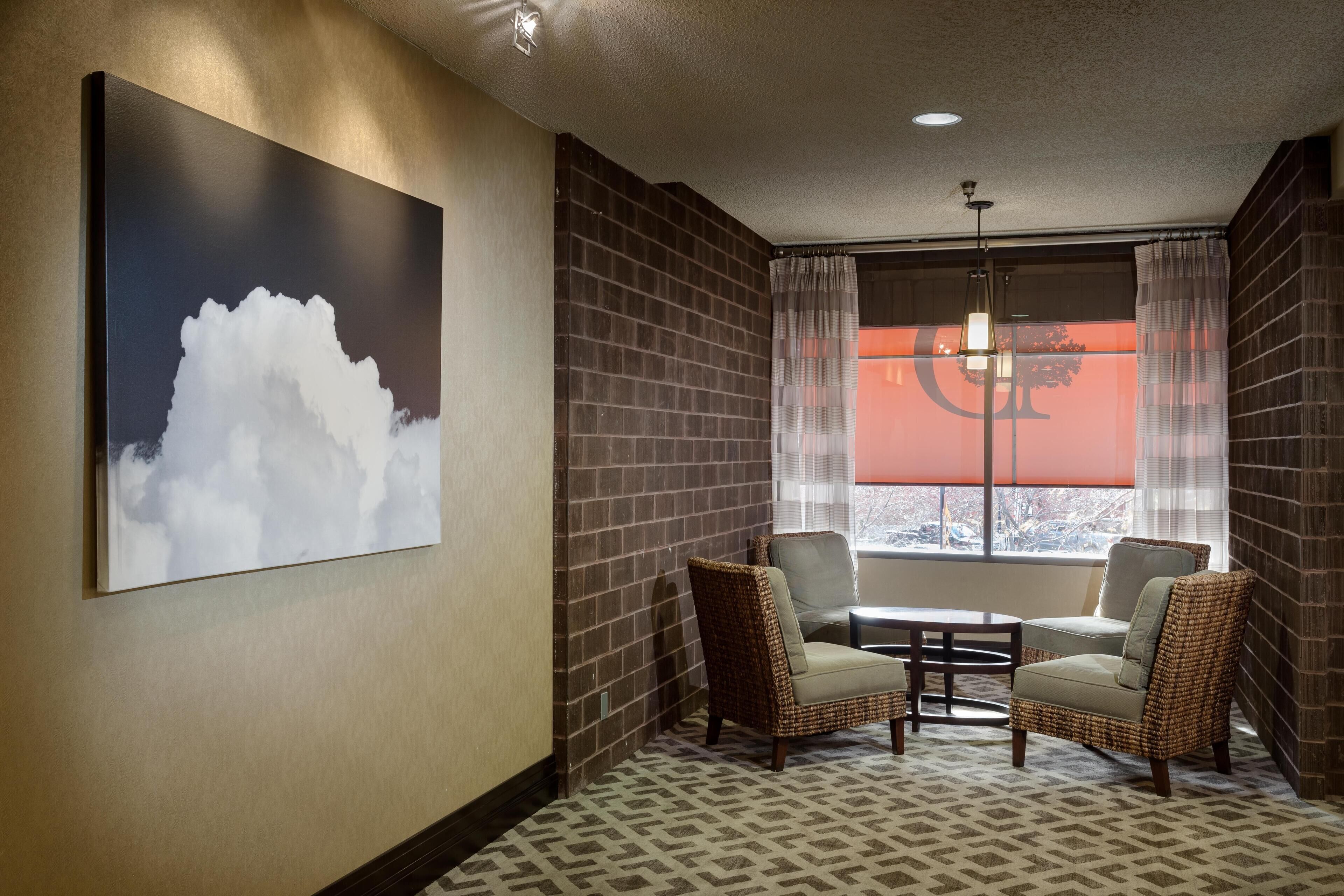 Habitación de hotel con un cuadro abstracto grande, dos sillas de mimbre, una mesita y una ventana con cortinas.