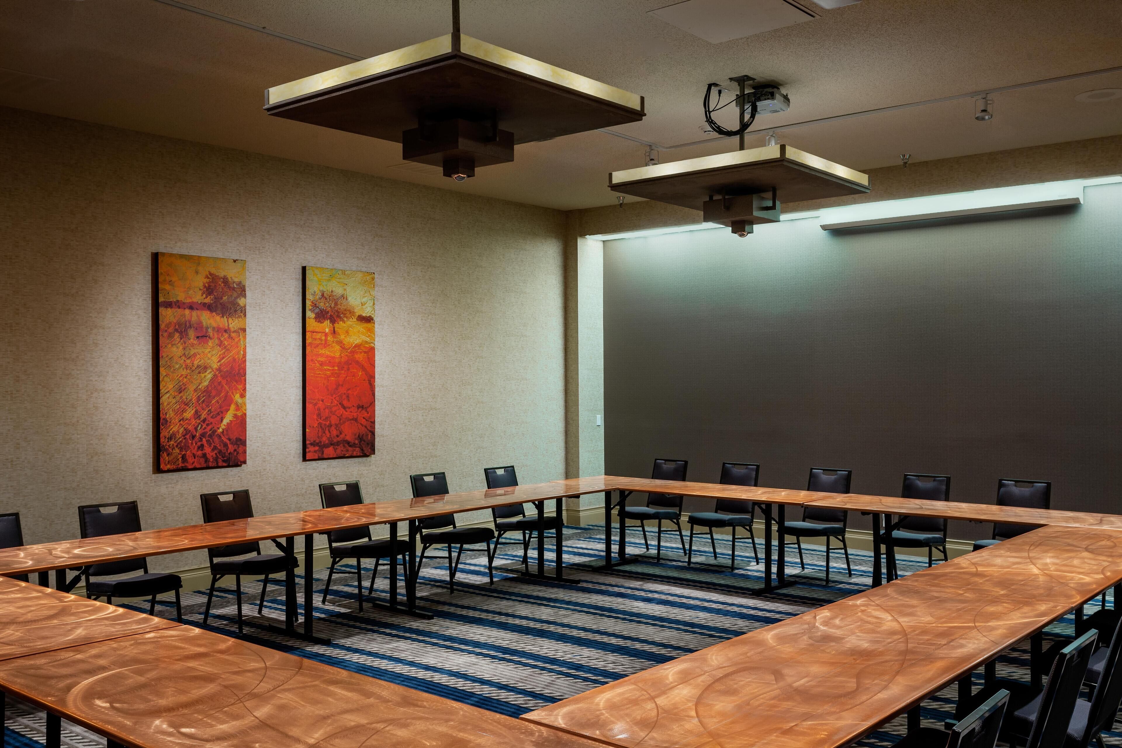 Uma sala de conferências com uma mesa comprida, cadeiras e duas pinturas abstratas na parede.