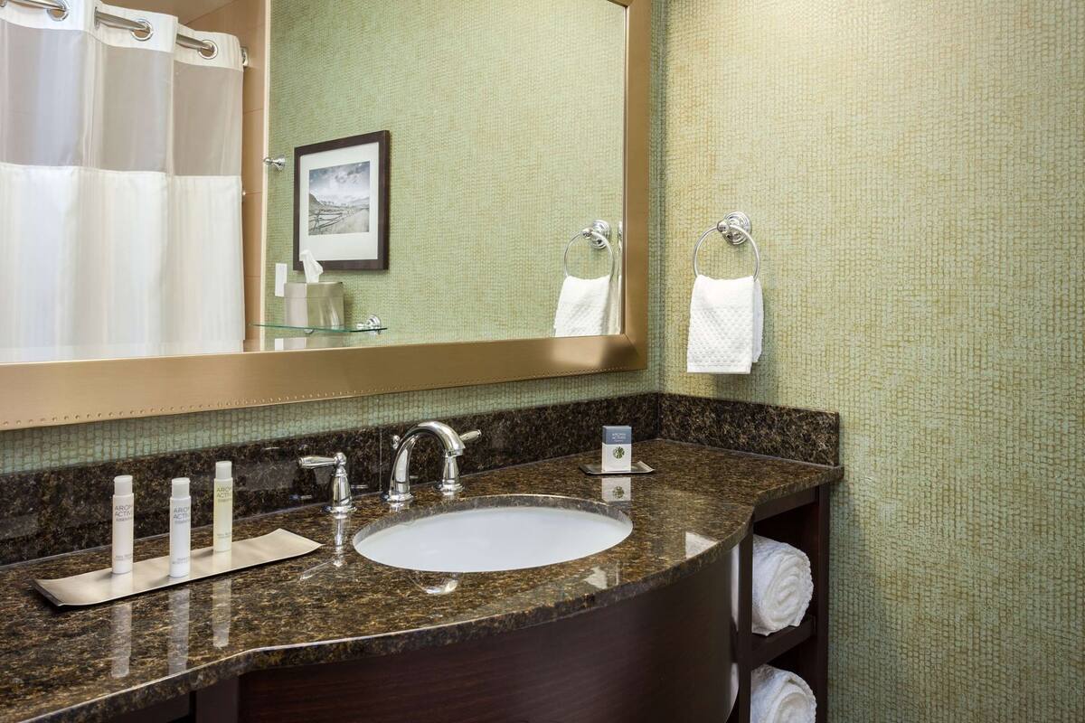 A bathroom with a granite countertop sink, a mirror, and a towel rack.