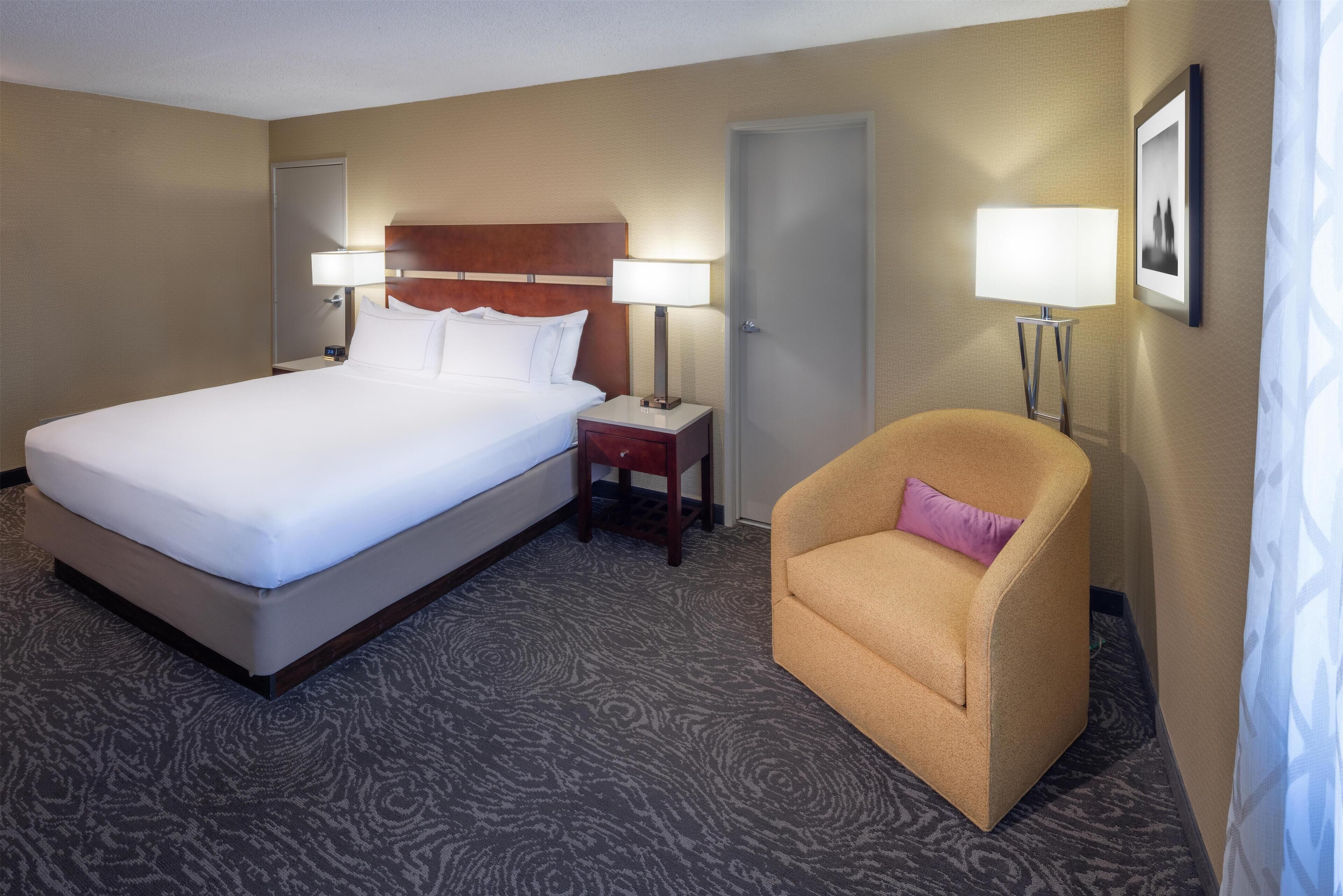 Une chambre d’hôtel avec un grand lit, deux tables de chevet avec des lampes, une chaise et une porte.