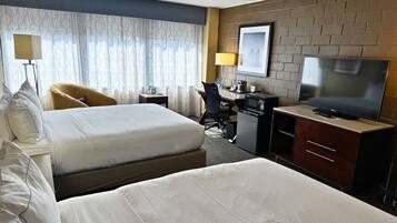 Habitación de hotel con una cama grande, un escritorio con computadora, televisor y ventana con cortinas.