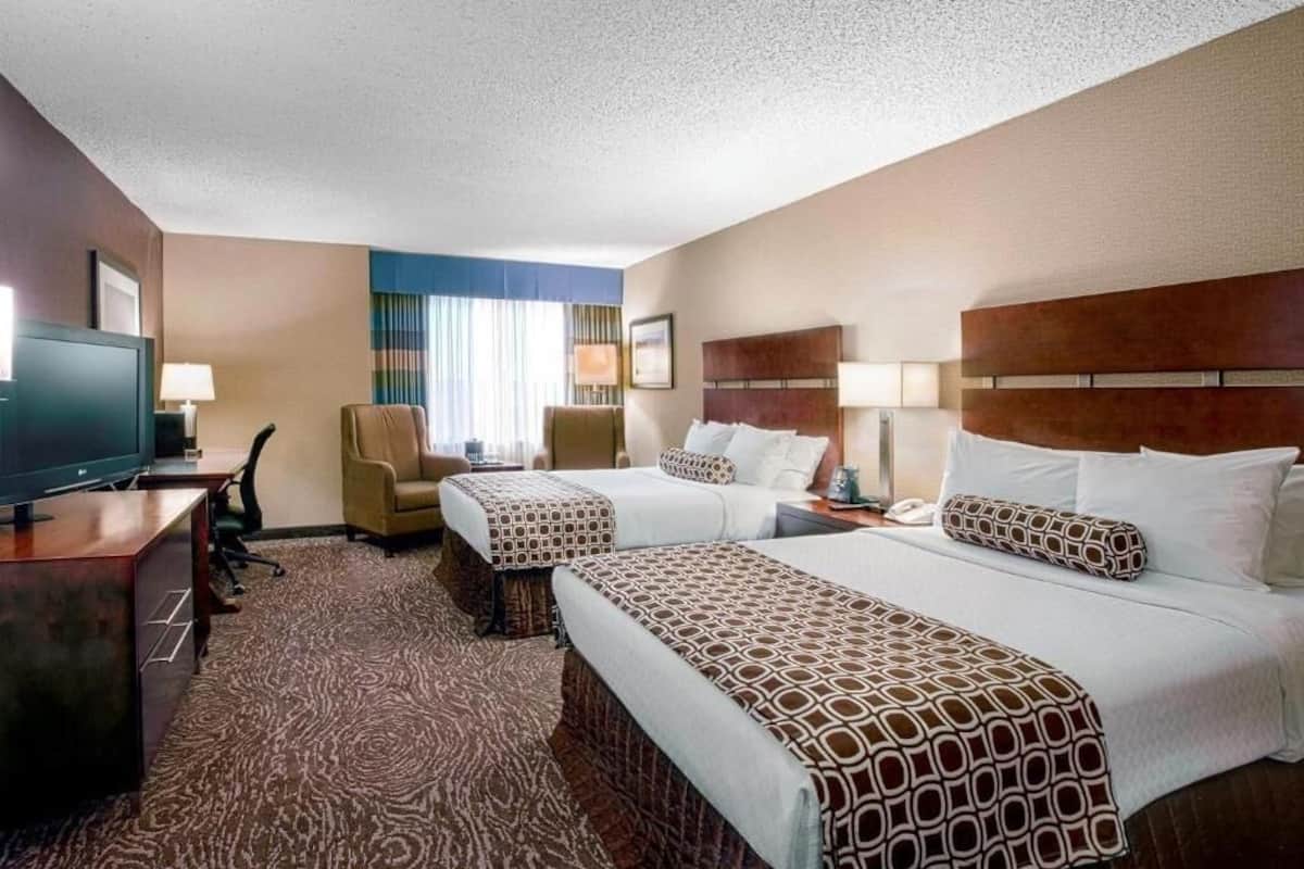 A hotel room with two beds, a desk with a television, a chair, and a window with curtains.