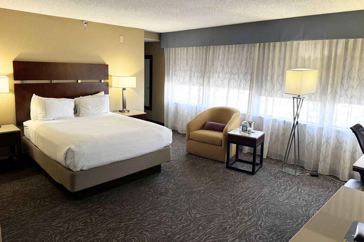 A hotel room with a large bed, a chair, a desk, and a lamp.