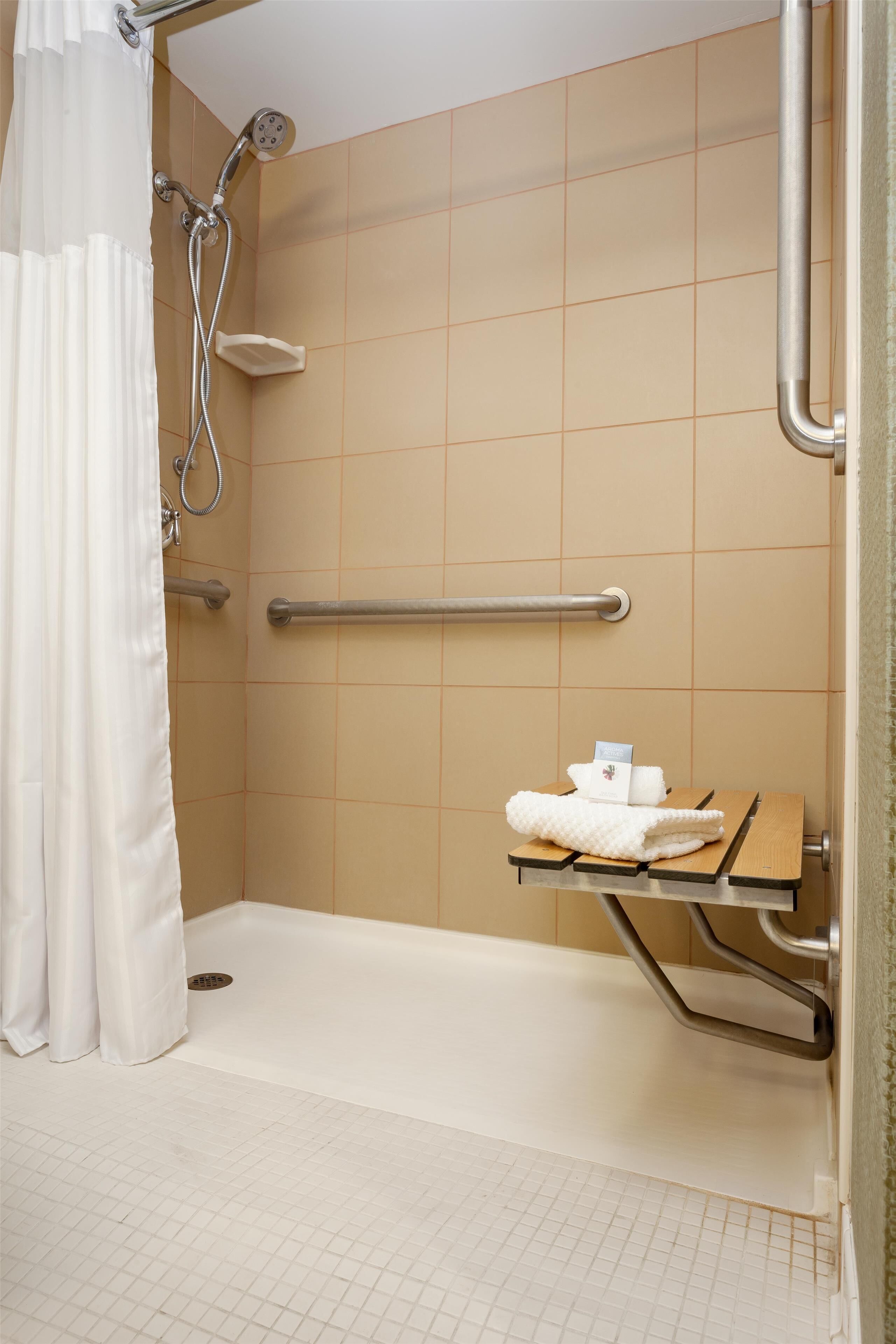 A shower area with a grab bar, a bench with towels, and a showerhead.