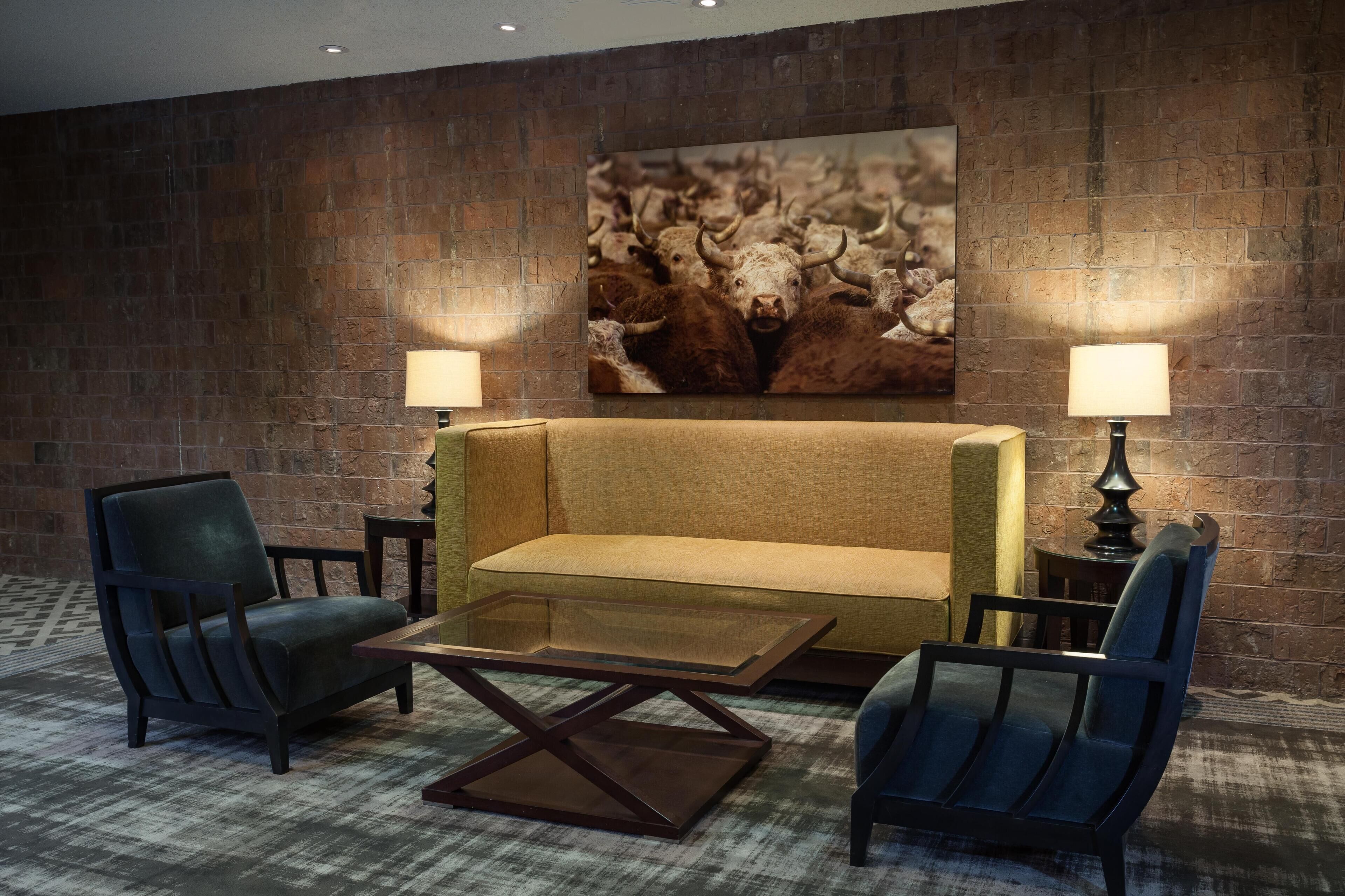 Una habitación con pared de ladrillo, un sofá, dos sillones, una mesa de centro y dos lámparas.