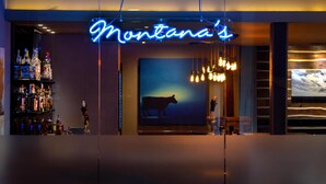 A bar area with a neon sign reading "Montana's," a bar stocked with liquor bottles, and a large screen displaying a cow silhouette. - DoubleTree by Hilton Hotel Billings (Billings)