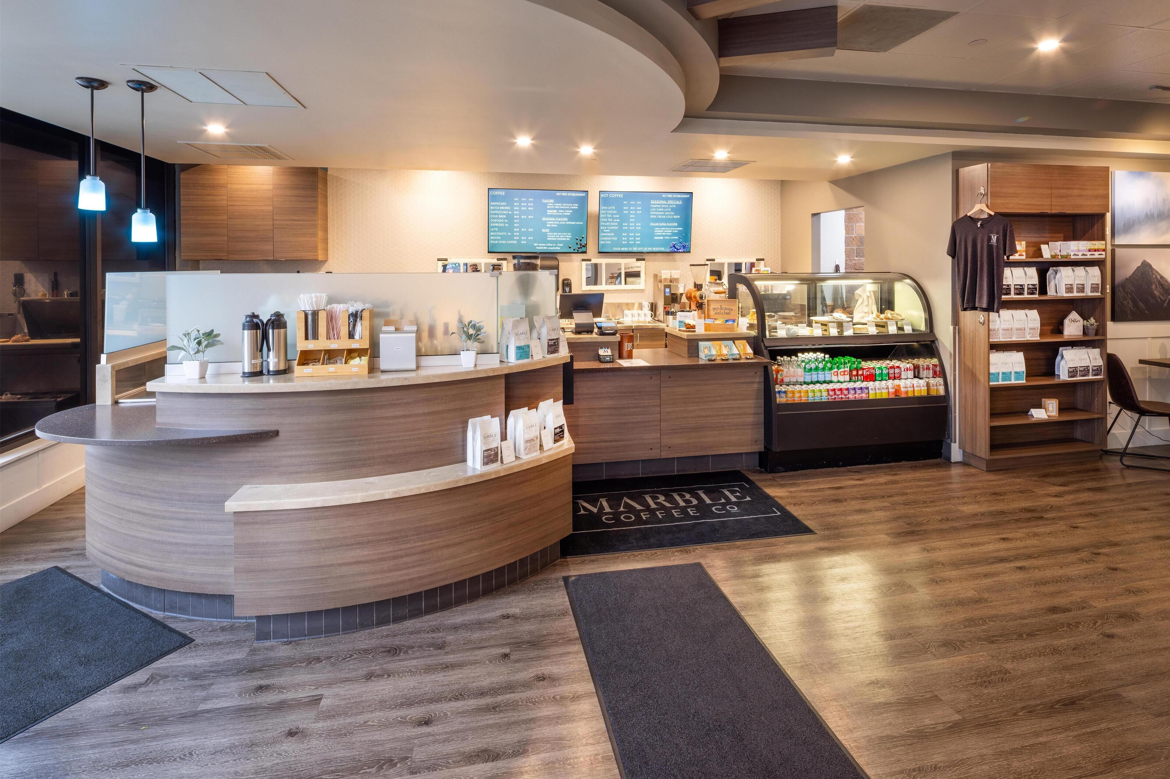 L’intérieur d’un café moderne présente un comptoir d’accueil incurvé, des écrans numériques affichant le menu et un présentoir où sont exposés les produits à base de café.