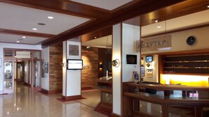 A reception area with a wooden reception desk, a digital screen, and a sign indicating the reception. - Mercure Bad Duerkheim an den Salinen (Bad Durkheim)