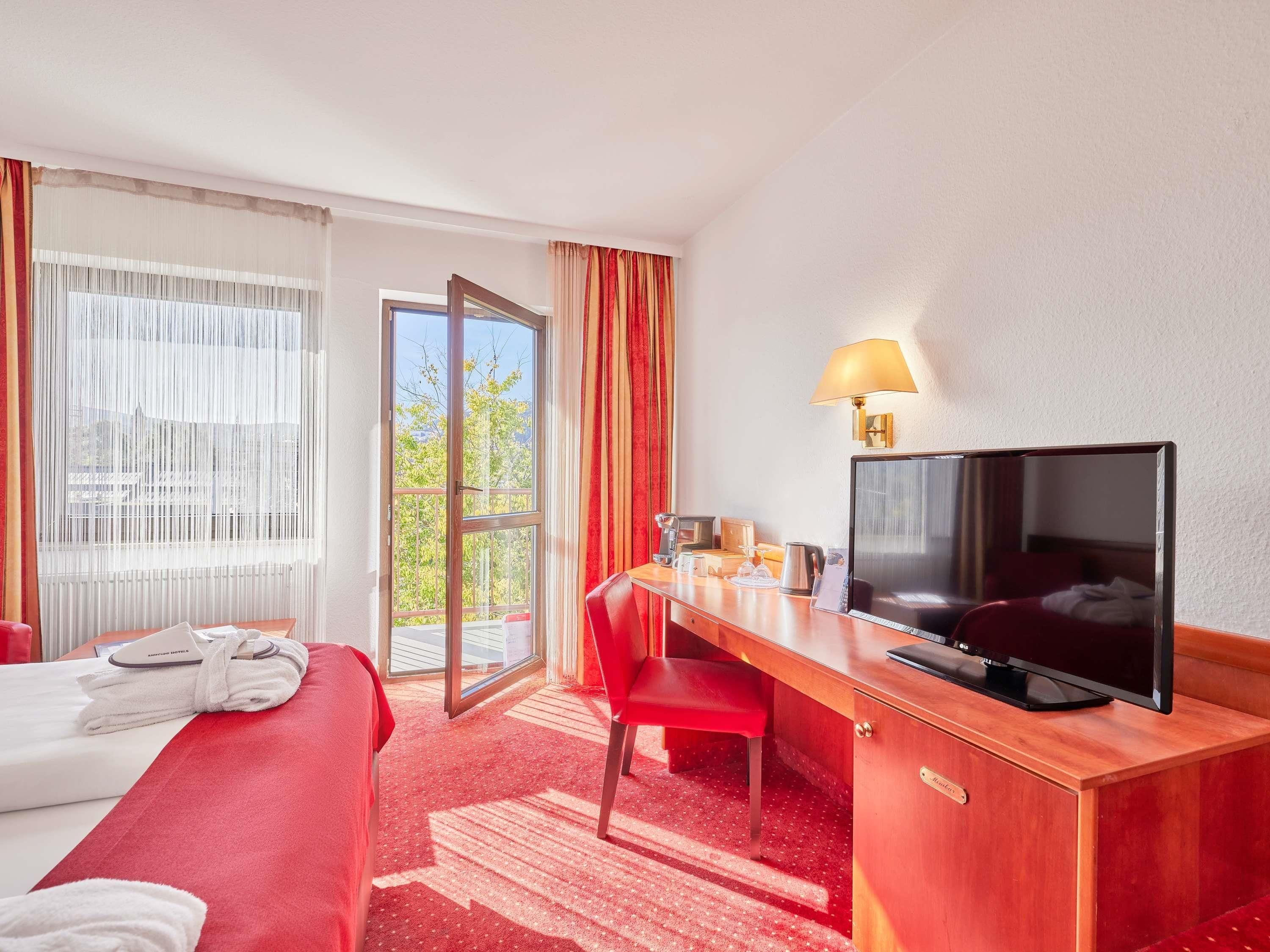 A hotel room with a bed, a desk, a television, and a window with curtains.