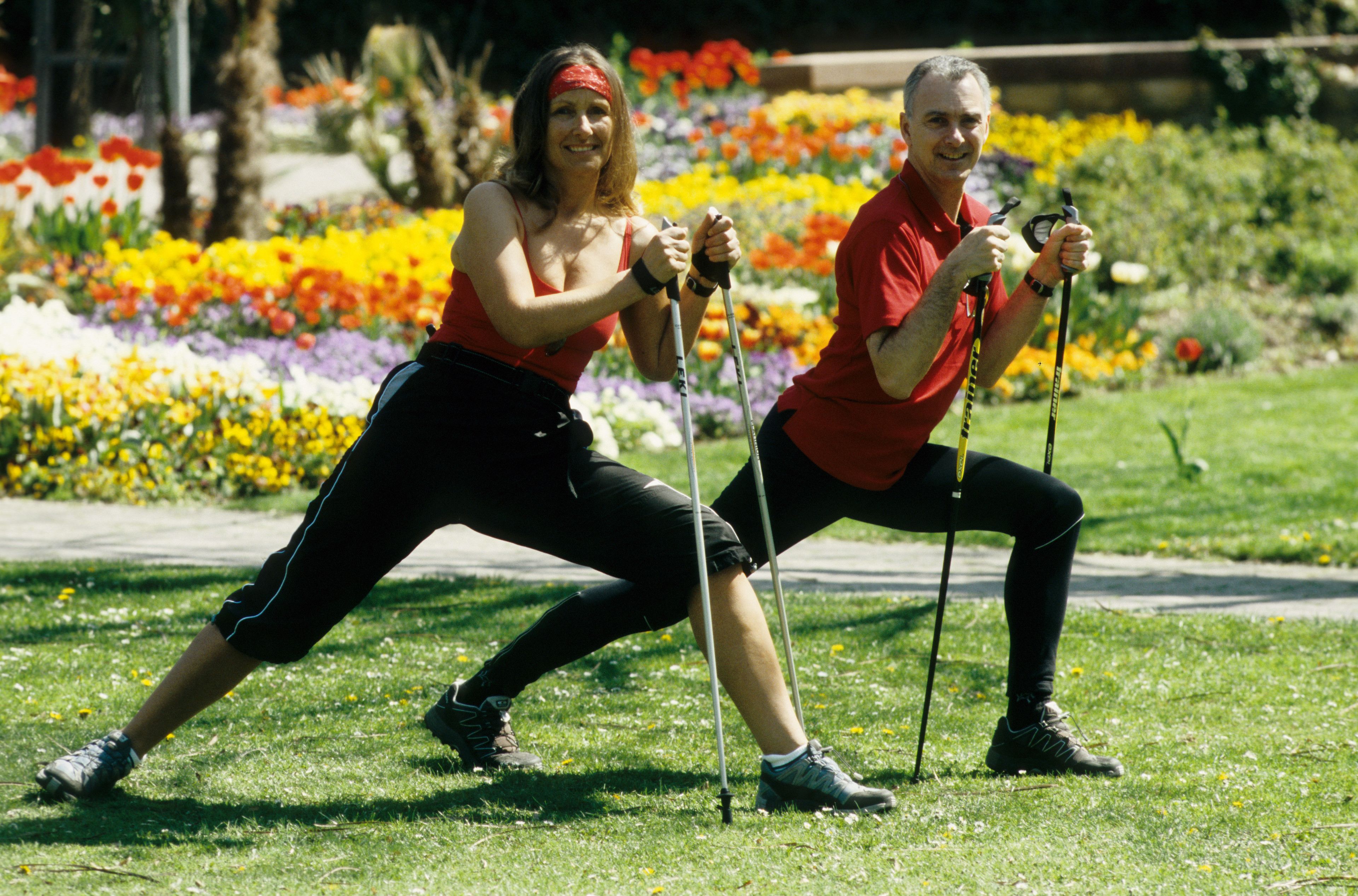 Dos personas usando bastones de senderismo en un jardín con flores coloridas.