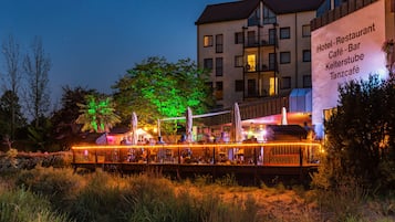 A waterfront restaurant with outdoor seating, a building with balconies, and a sign indicating it is a hotel, restaurant, café, bar, and a place called 'Kelterstube'.