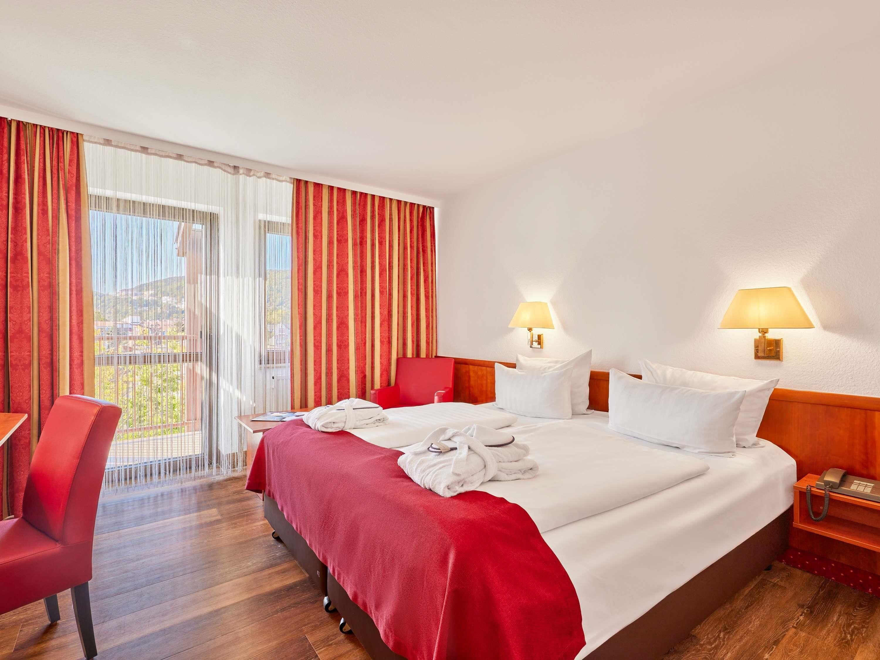 Una habitación de hotel con cama, escritorio, silla y balcón con cortinas.
