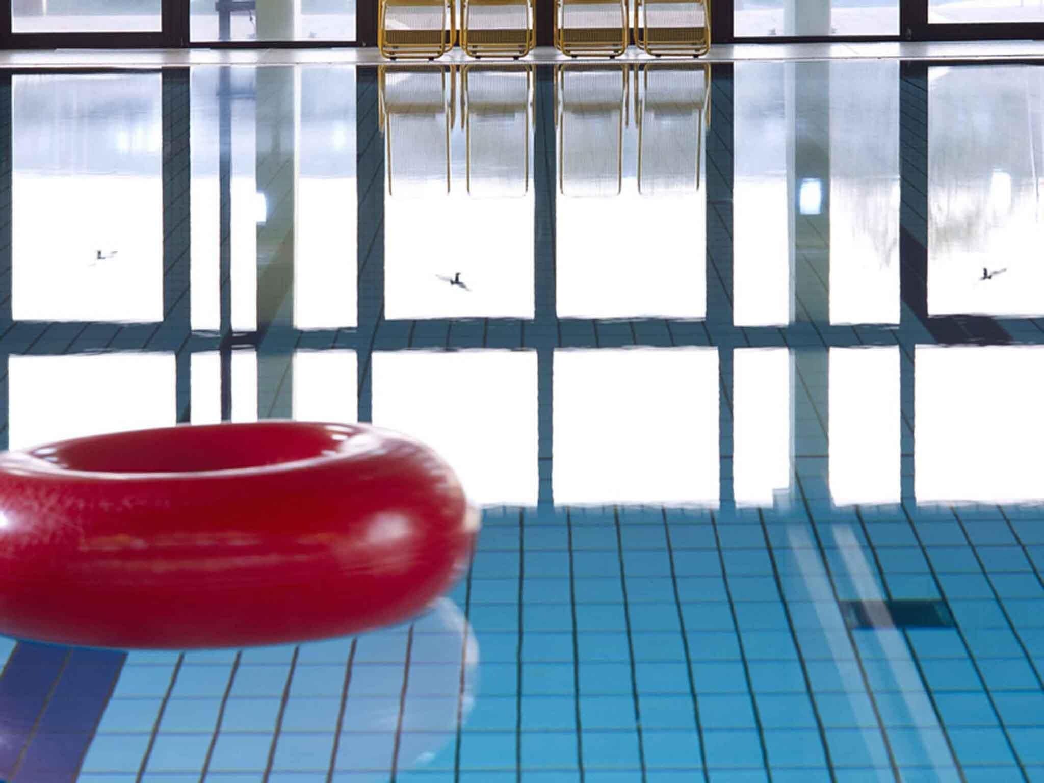 A swimming pool with a red ring buoy, tiled floor, and a reflection of a building with windows and a balcony.