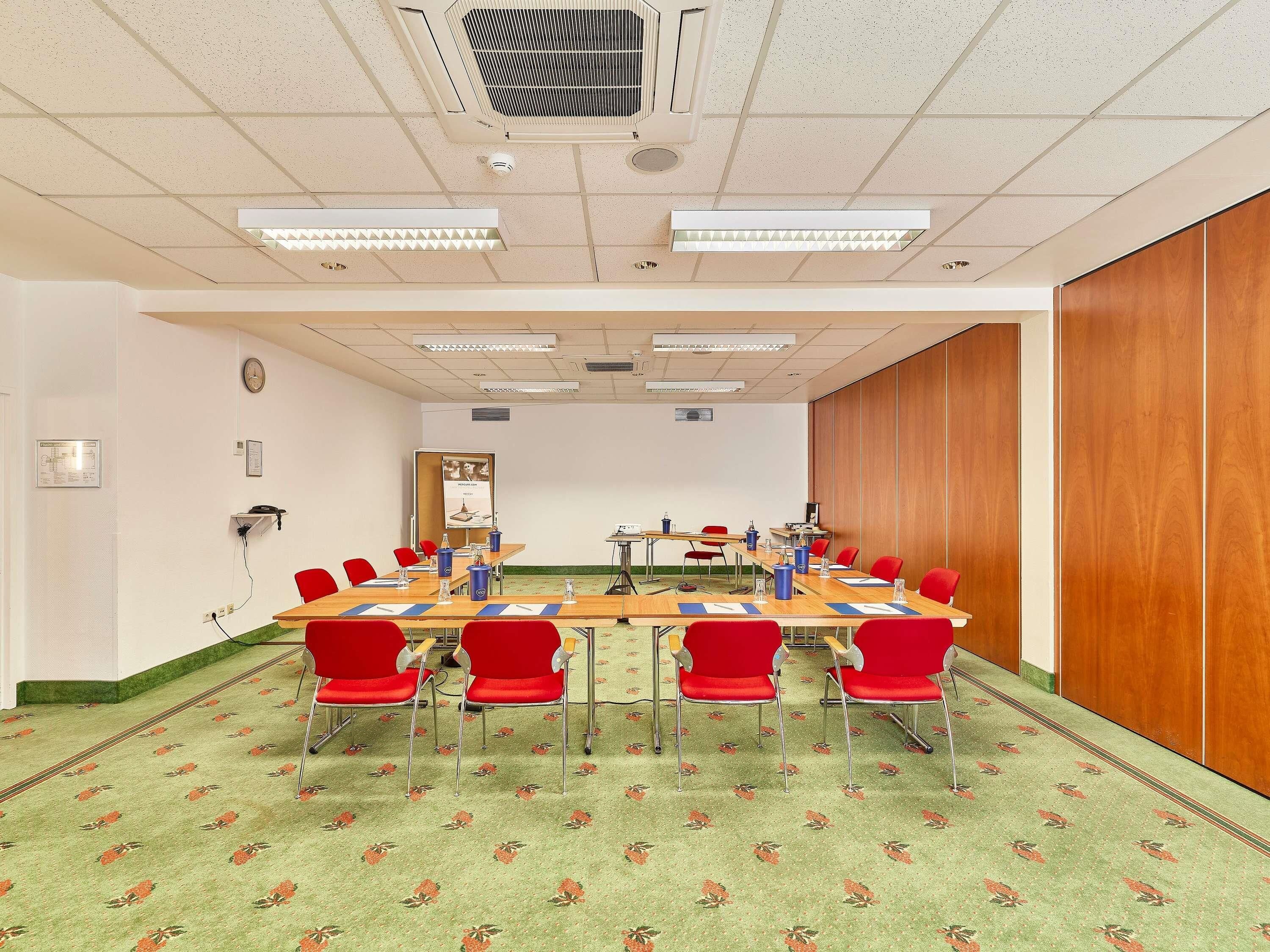 A conference room with a long table, red chairs, and a patterned carpet.