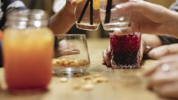A group of people holding glasses with straws, a jar of nuts, and a glass of red drink on a table.