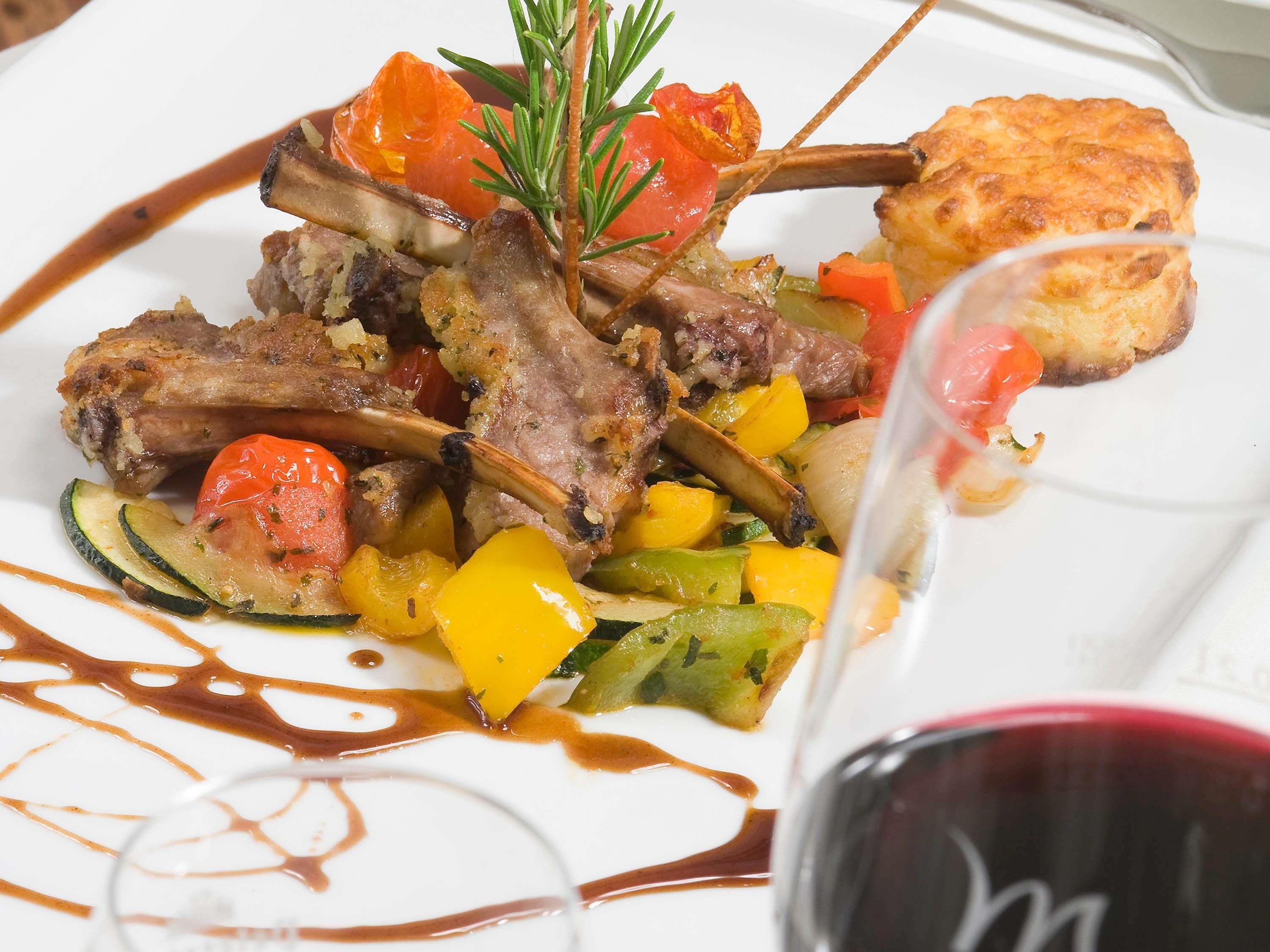 A plate of food with lamb chops, vegetables, and a sauce.