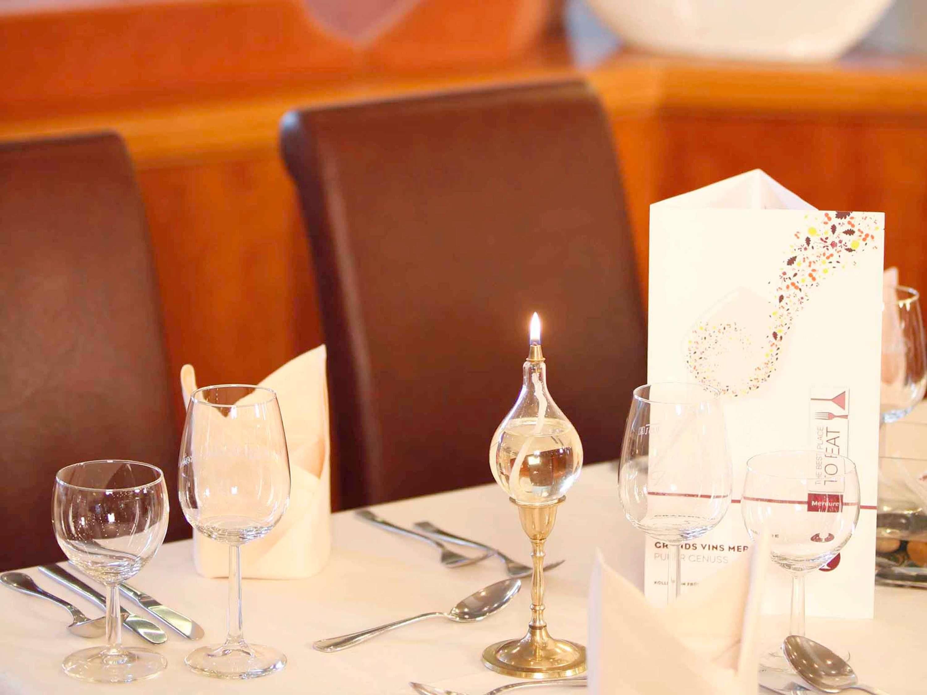 Une table dressée avec des verres à vin, une bougie et un menu.