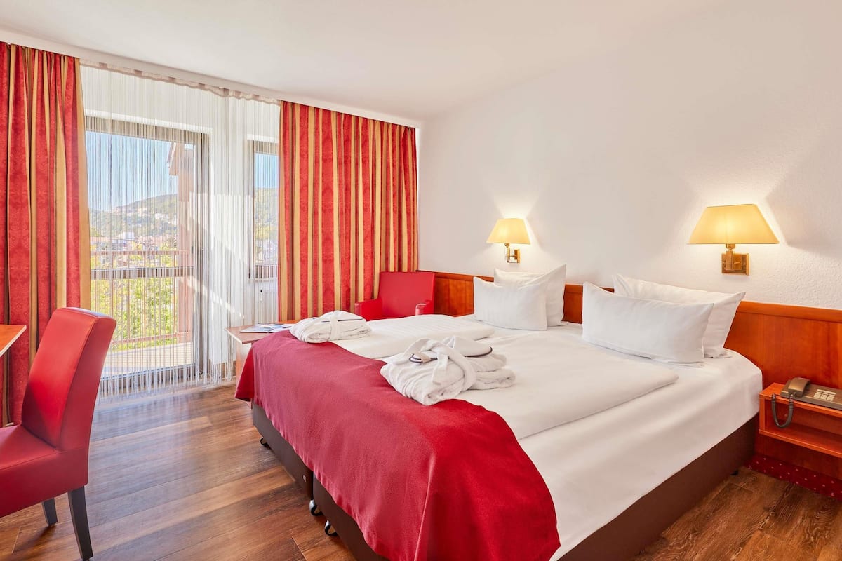 Een hotelkamer met een bed, een bureau, een stoel en een balkon met gordijnen.